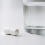 Doorslikbare capsule met maagballon naast een glas water op witte ondergrond