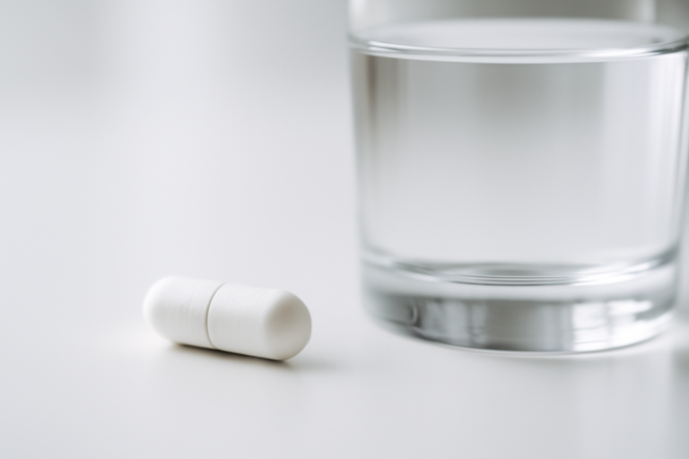 Doorslikbare capsule met maagballon naast een glas water op witte ondergrond